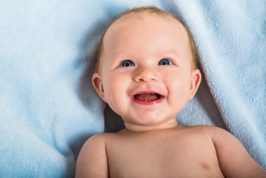 Lachendes Baby liegt auf einer hellblauen Decke und blickt nach oben.